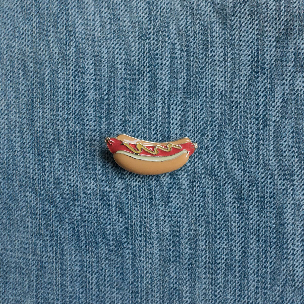 Hot dog enamel pin with ketchup and mustard on denim fabric background