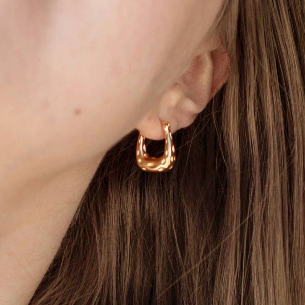 Close-up of a gold textured hoop earring worn on an ear with light brown hair