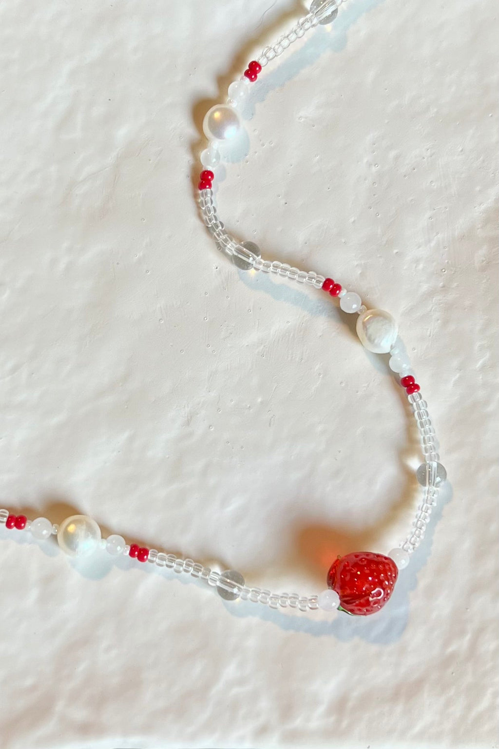 Beaded necklace with clear, white, and red beads featuring a strawberry charm on a white background