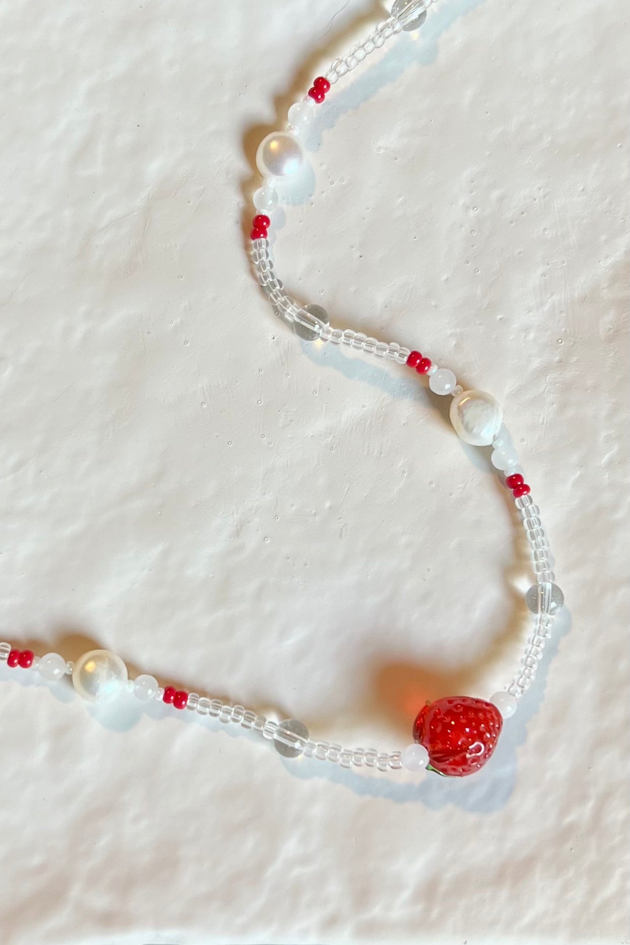 Beaded necklace with clear, white, and red beads featuring a strawberry charm on a white background
