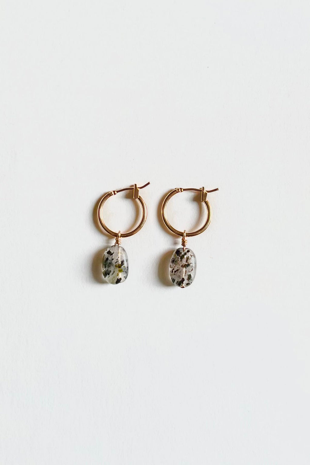Gold hoop earrings with oval dalmatian jasper gemstone charms on white background