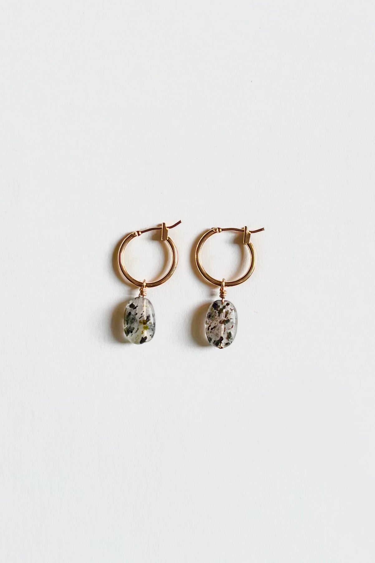 Gold hoop earrings with oval dalmatian jasper gemstone charms on white background