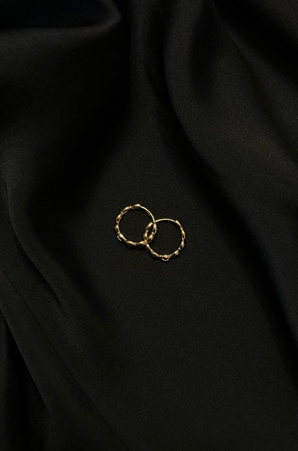 Gold hoop earrings with textured design on black silk fabric background