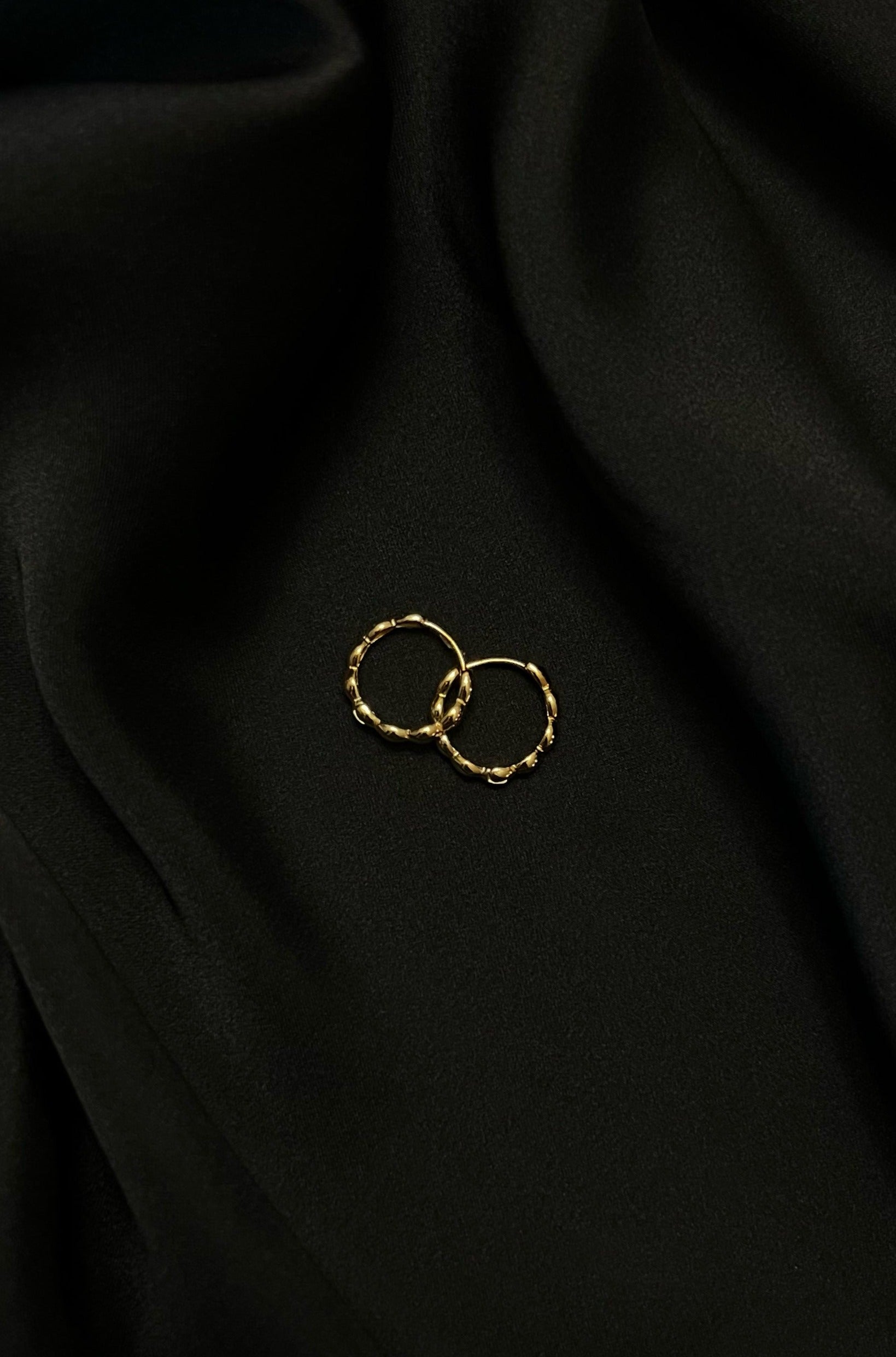 Gold hoop earrings with textured design on black silk fabric background