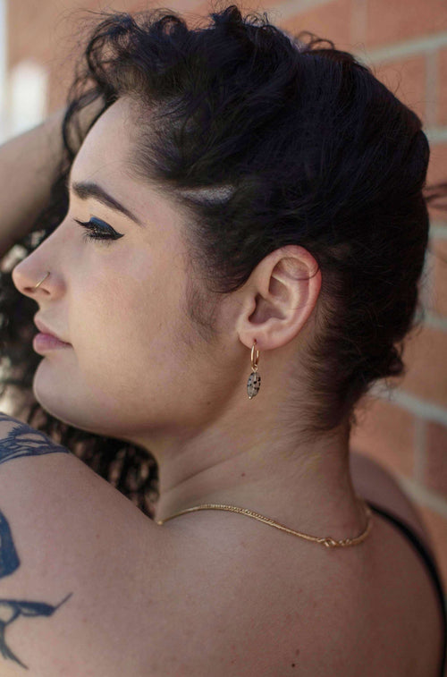 Woman wearing gold Dalmatian print hoop earrings, gold necklace, and nose ring outdoors