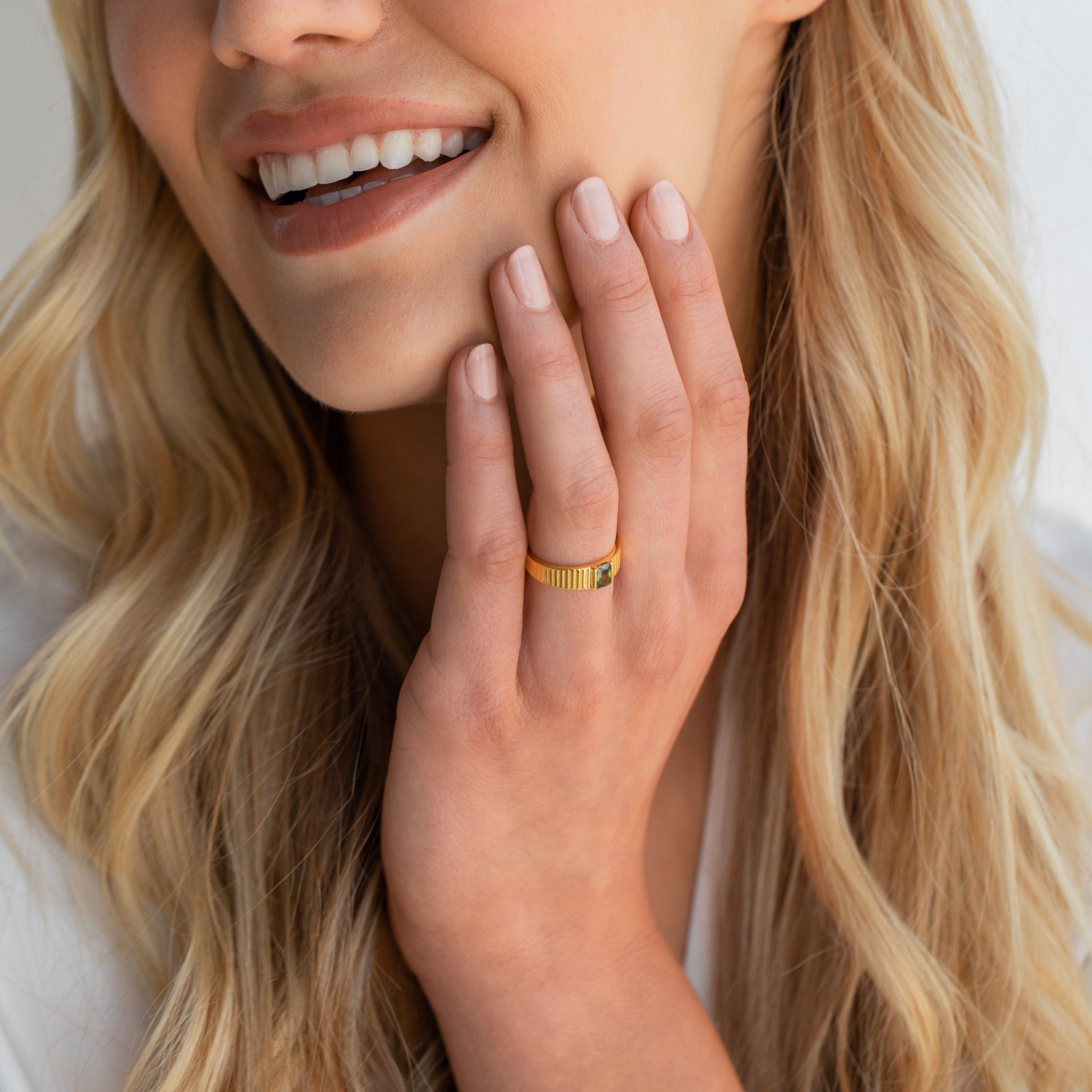 Smiling woman wearing gold band ring with gemstone, close-up jewelry detail