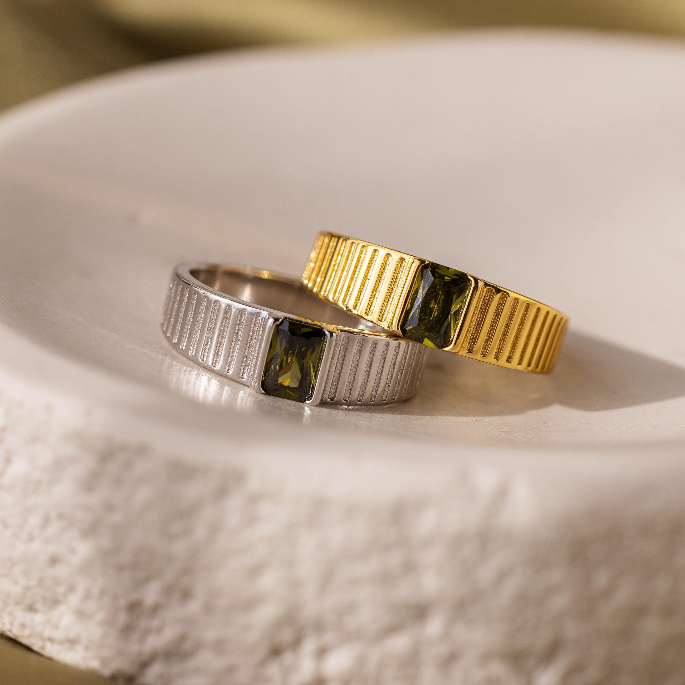 Gold and silver rings with rectangular green gemstones on a ceramic dish