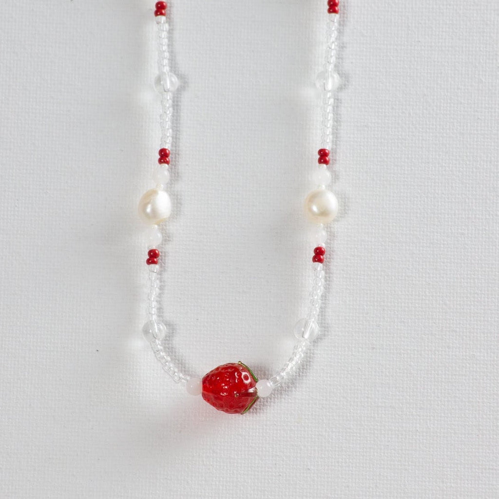 Beaded necklace with a red strawberry charm, pearl and glass beads on white background