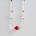 Beaded necklace with a red strawberry charm, pearl and glass beads on white background