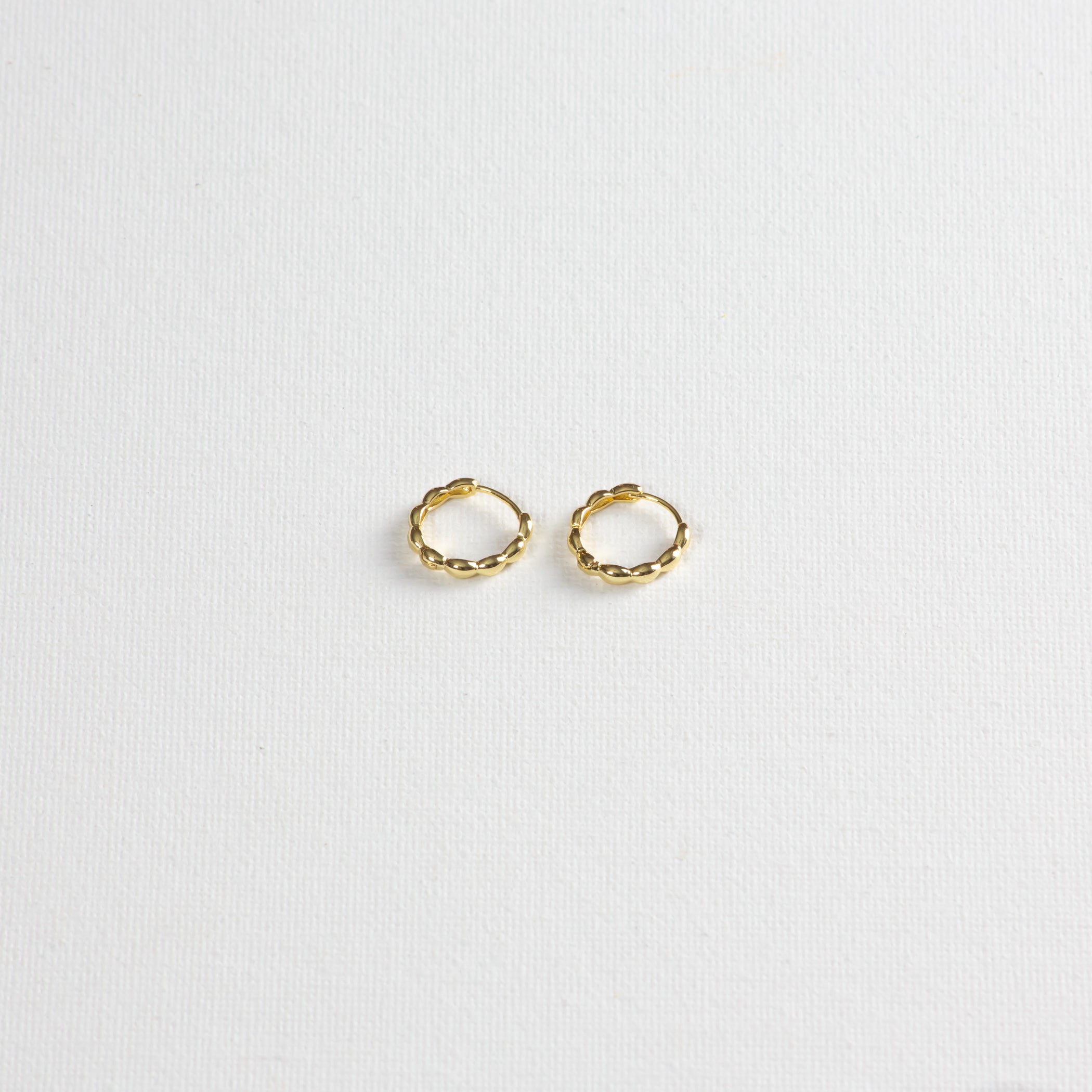Pair of small gold twisted hoop earrings on a white textured background