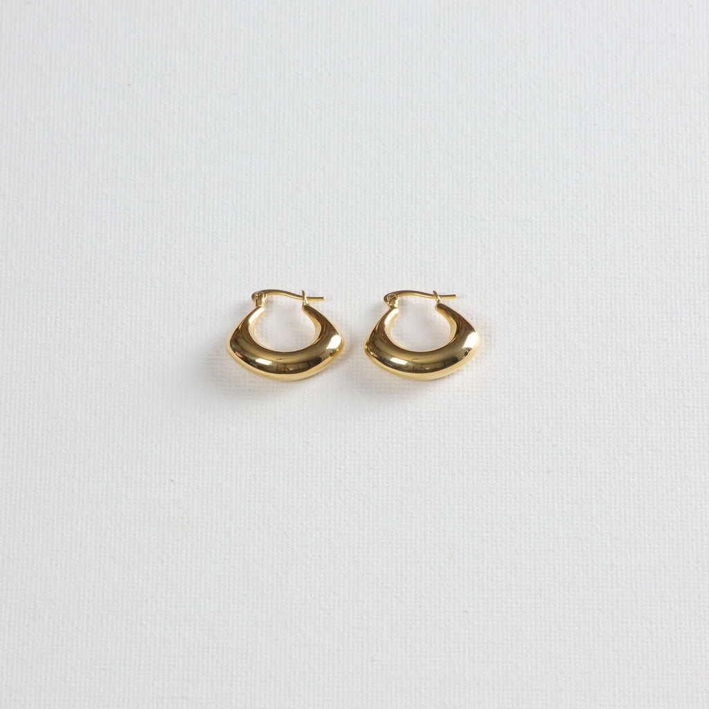 Gold chunky hoop earrings with smooth finish on white textured background