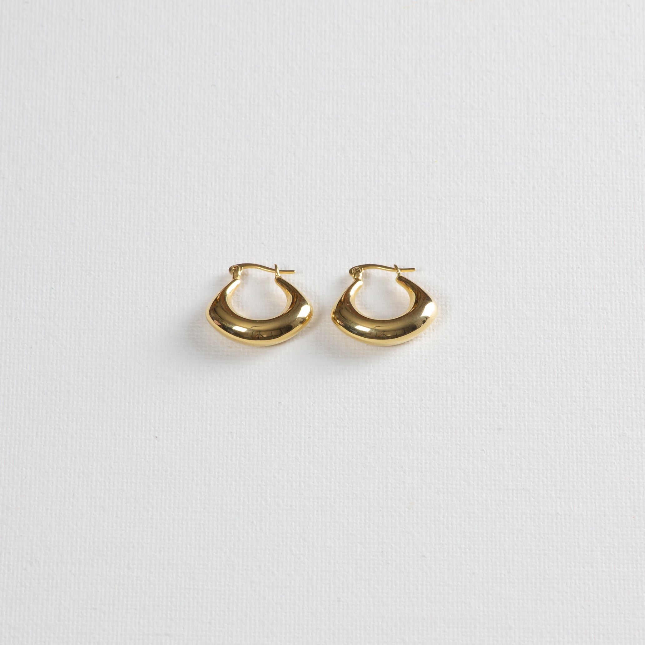 Gold chunky hoop earrings with smooth finish on white textured background