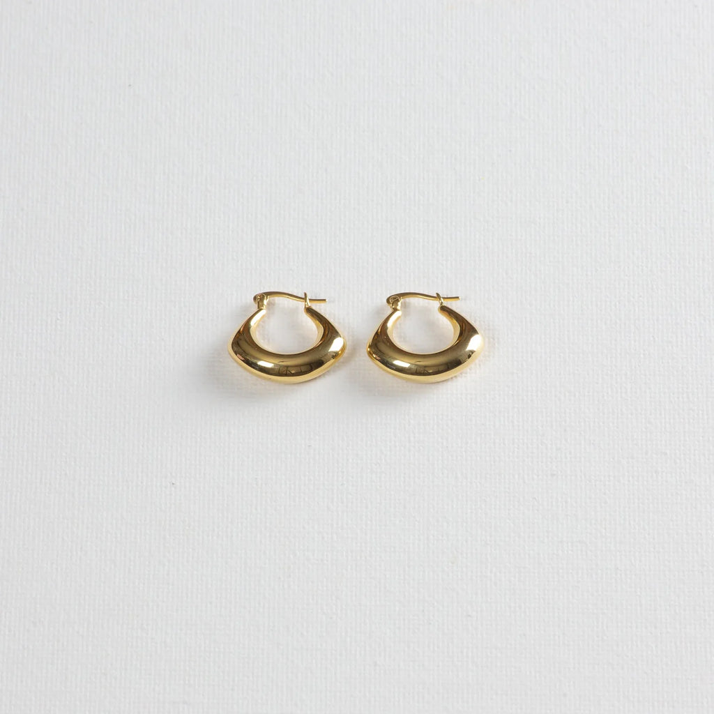 Pair of chunky gold hoop earrings on a white textured background