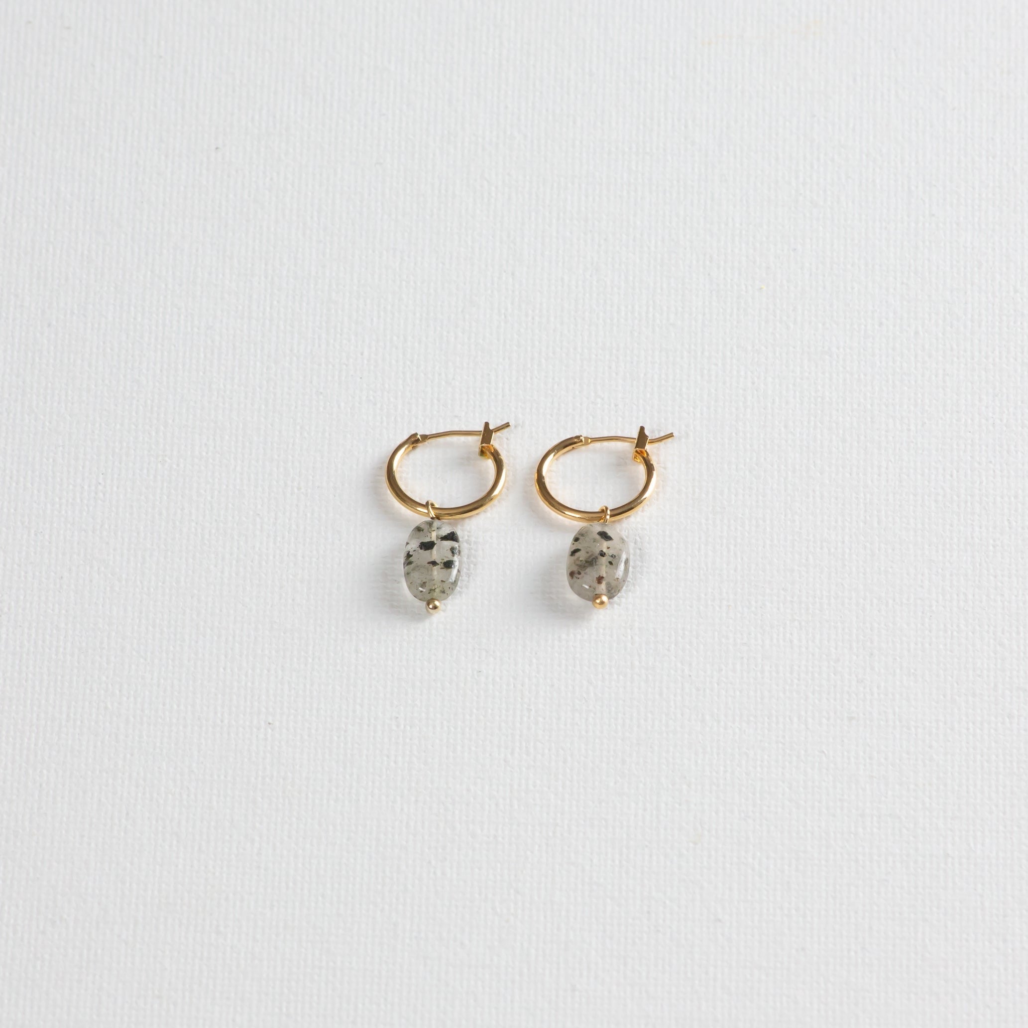Gold hoop earrings with oval dalmatian jasper stone charms on white background
