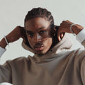 Man wearing beige hoodie, silver and pearl bracelets, neutral background, fashion portrait